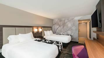 Habitación de hotel con dos camas, un escritorio, un televisor y una pared con diseño de rama de árbol.