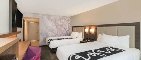 A hotel room with two beds, a desk, a TV, and a wall with a tree design.