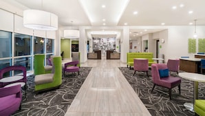 A modern lobby with a central reception desk, colorful seating areas, and a patterned carpet. - La Quinta Inn & Suites by Wyndham Mobile (Mobile)