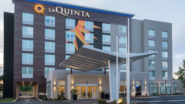 A La Quinta hotel with a modern facade, a prominent sun logo, and a covered entrance area. - La Quinta Inn & Suites by Wyndham Mobile (Mobile)