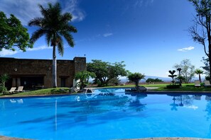 Una piscina azul cristalina con sillas de descanso, una palmera y un edificio de piedra con vistas a las montañas.