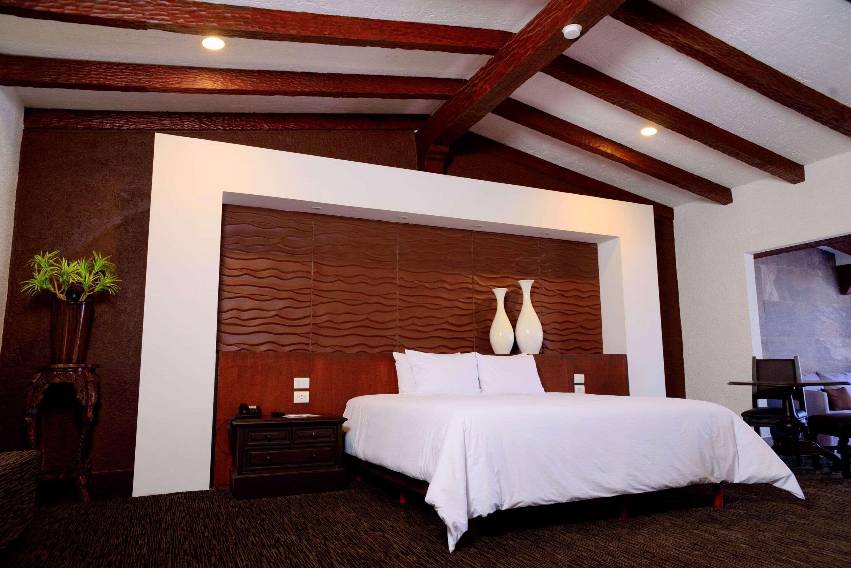 Un dormitorio con una cama grande, cabecero de madera, mesitas de noche y una planta en maceta.