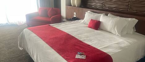 A hotel room with a large bed, red and white bedding, a red armchair, and a decorative wall panel.