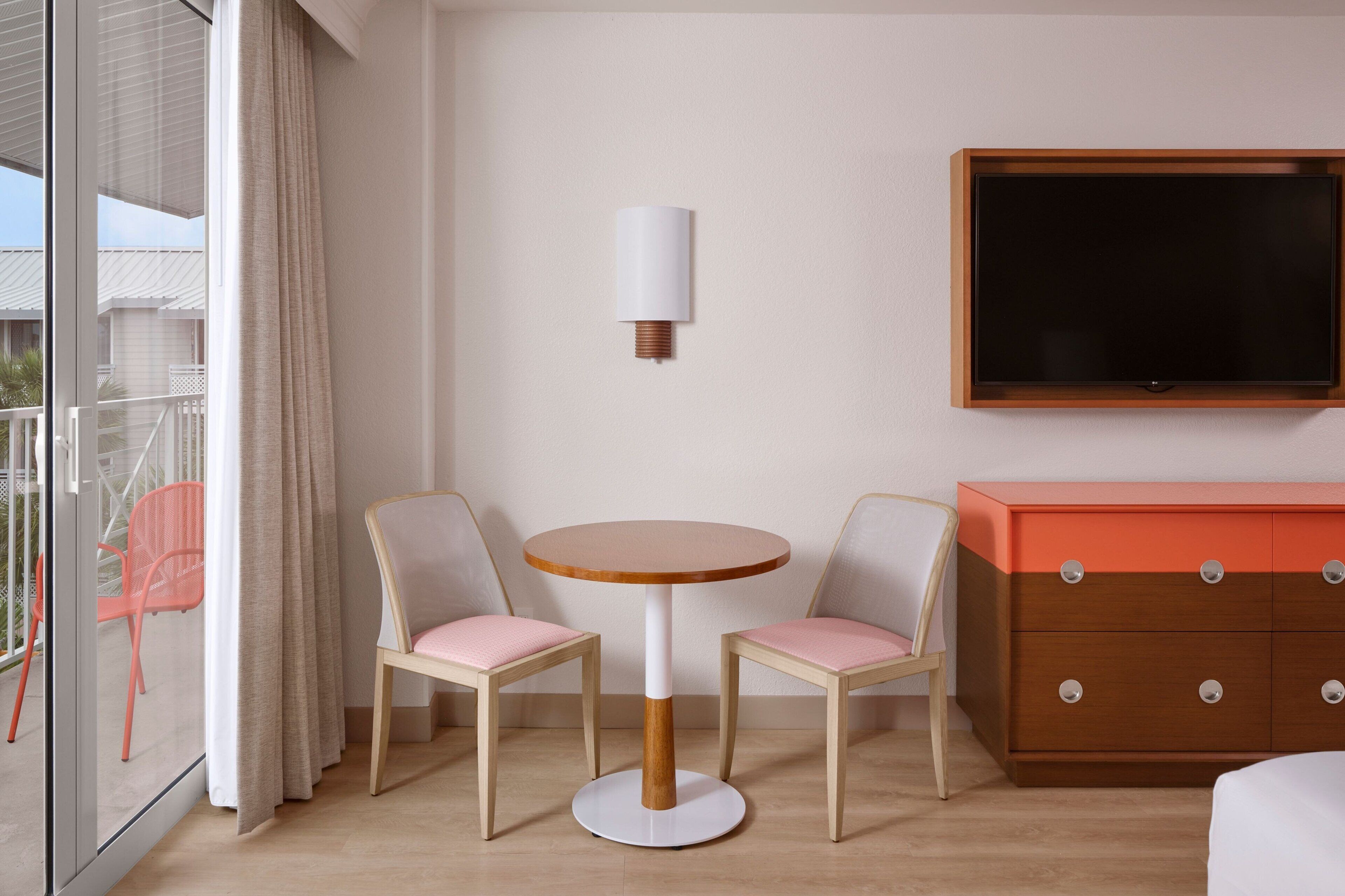Una habitación de hotel con una mesa redonda de madera, dos sillas, un televisor y un aparador de madera.