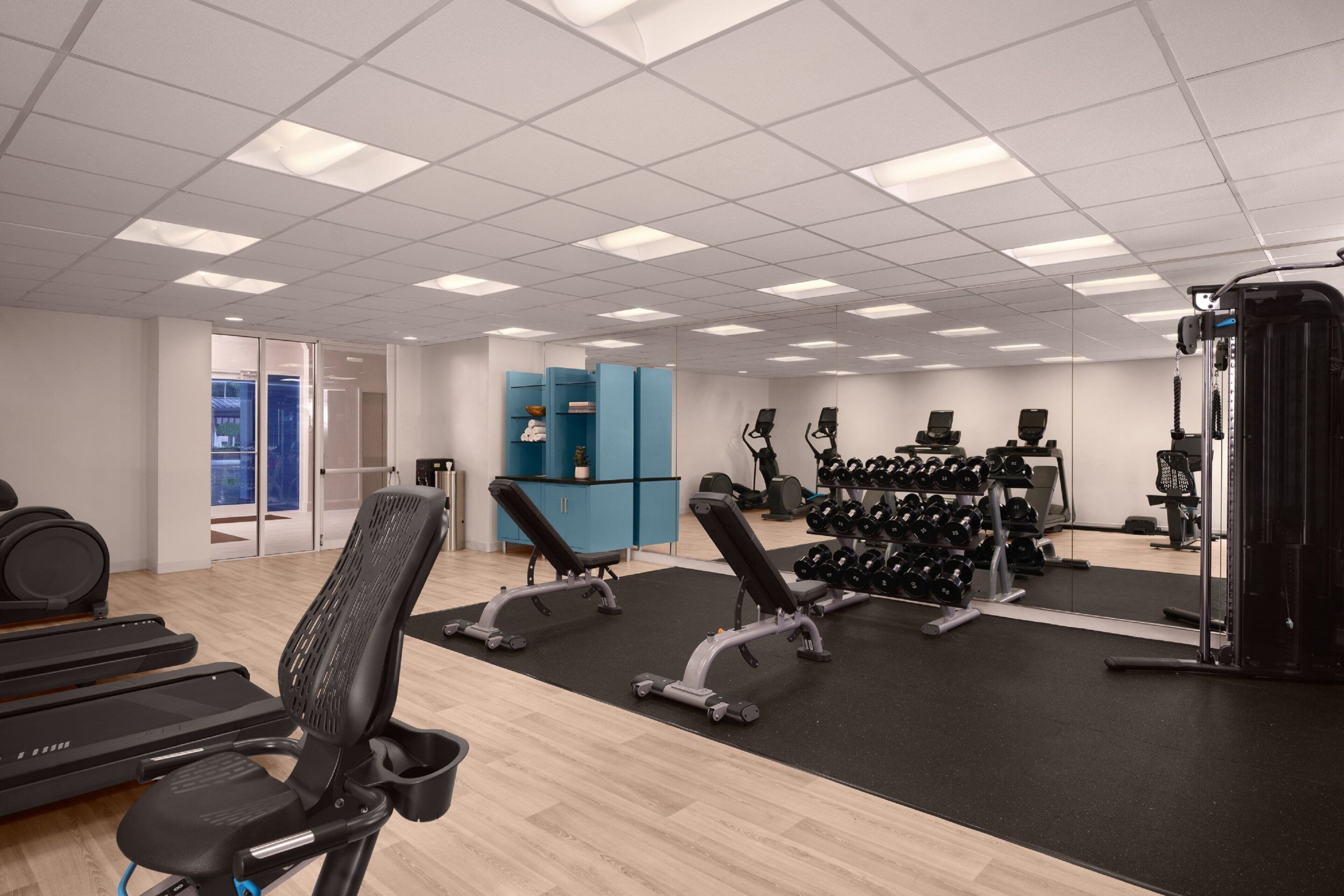 A modern gym with exercise equipment, a mirrored wall, and a blue cabinet.