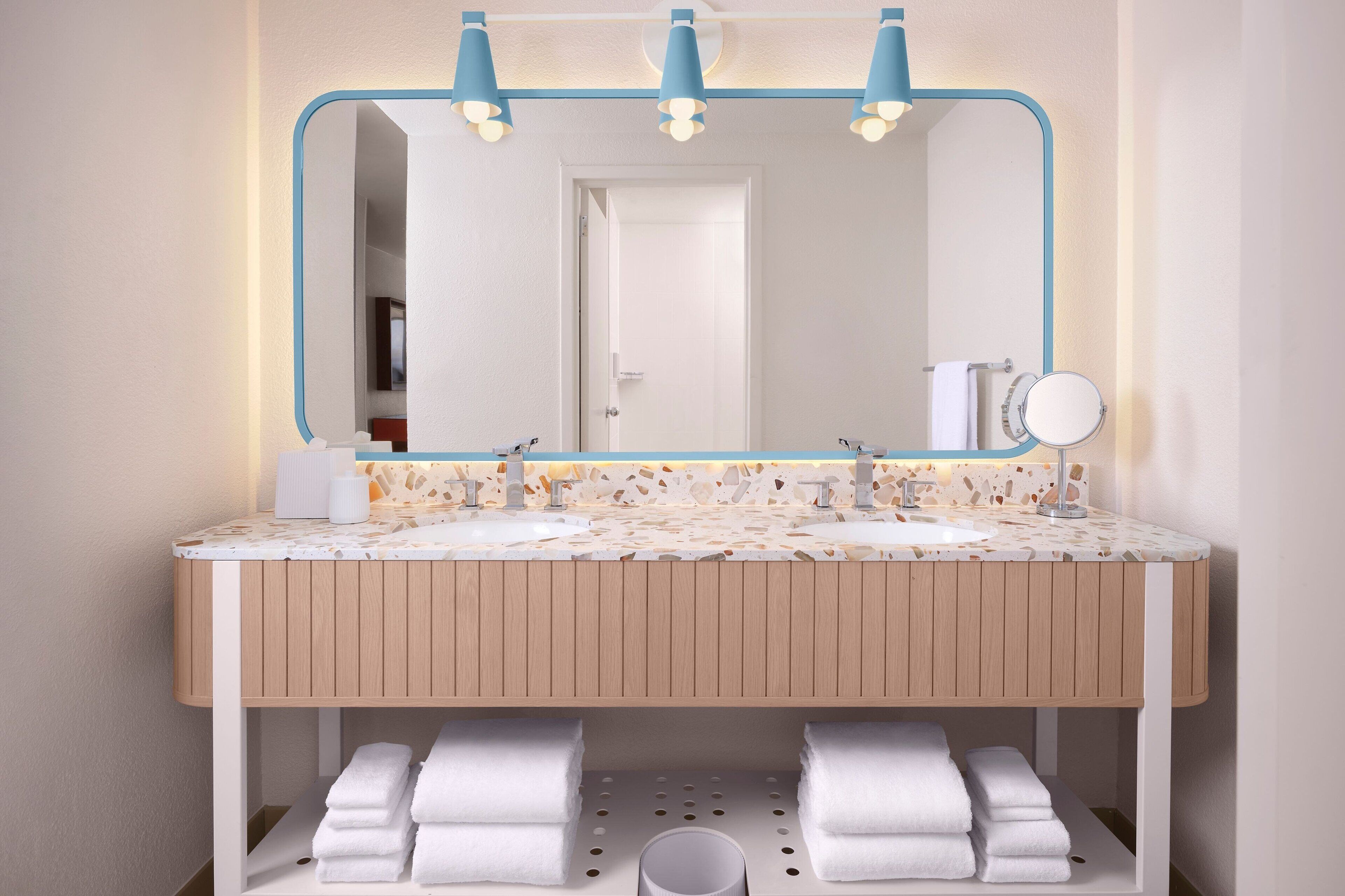 A bathroom with a wooden vanity, two sinks, a mirror with a blue frame, and a towel rack.