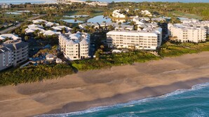Vista aérea de un resort costero con varias edificaciones, una playa y un puente al fondo.