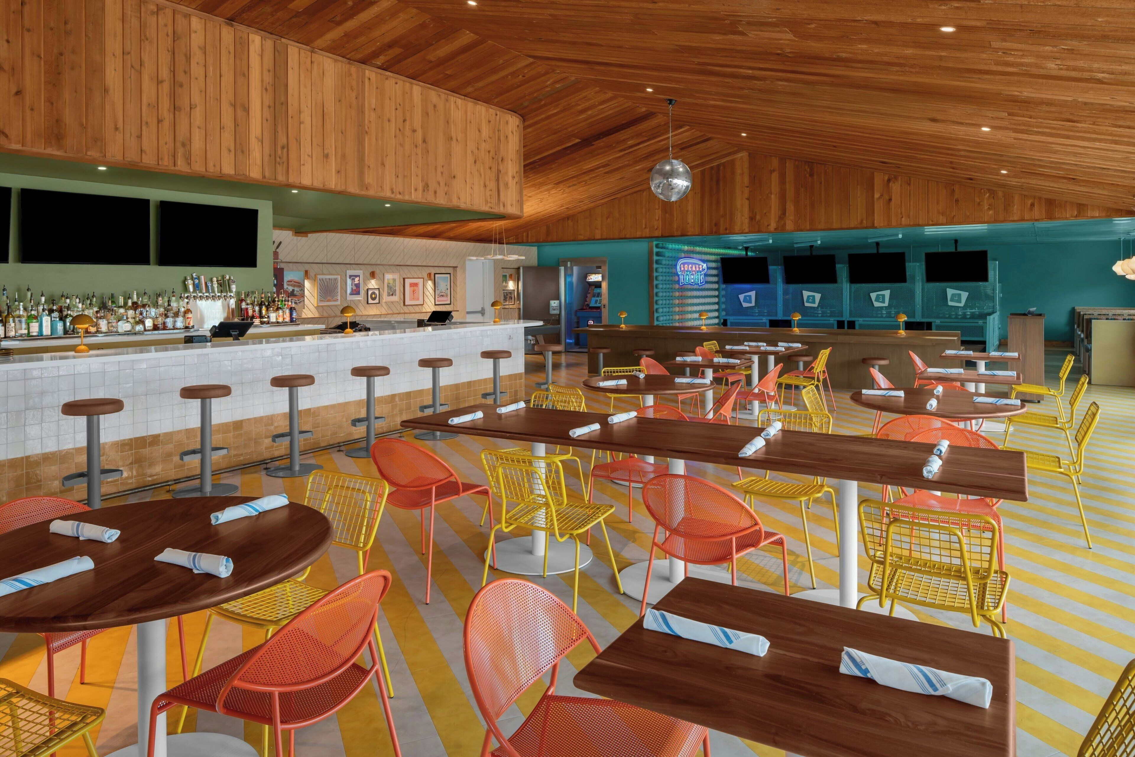 Amplio espacio interior con techo y paredes de madera, que incluye varias mesas y sillas, una zona de bar con mostrador y varias máquinas de juego.