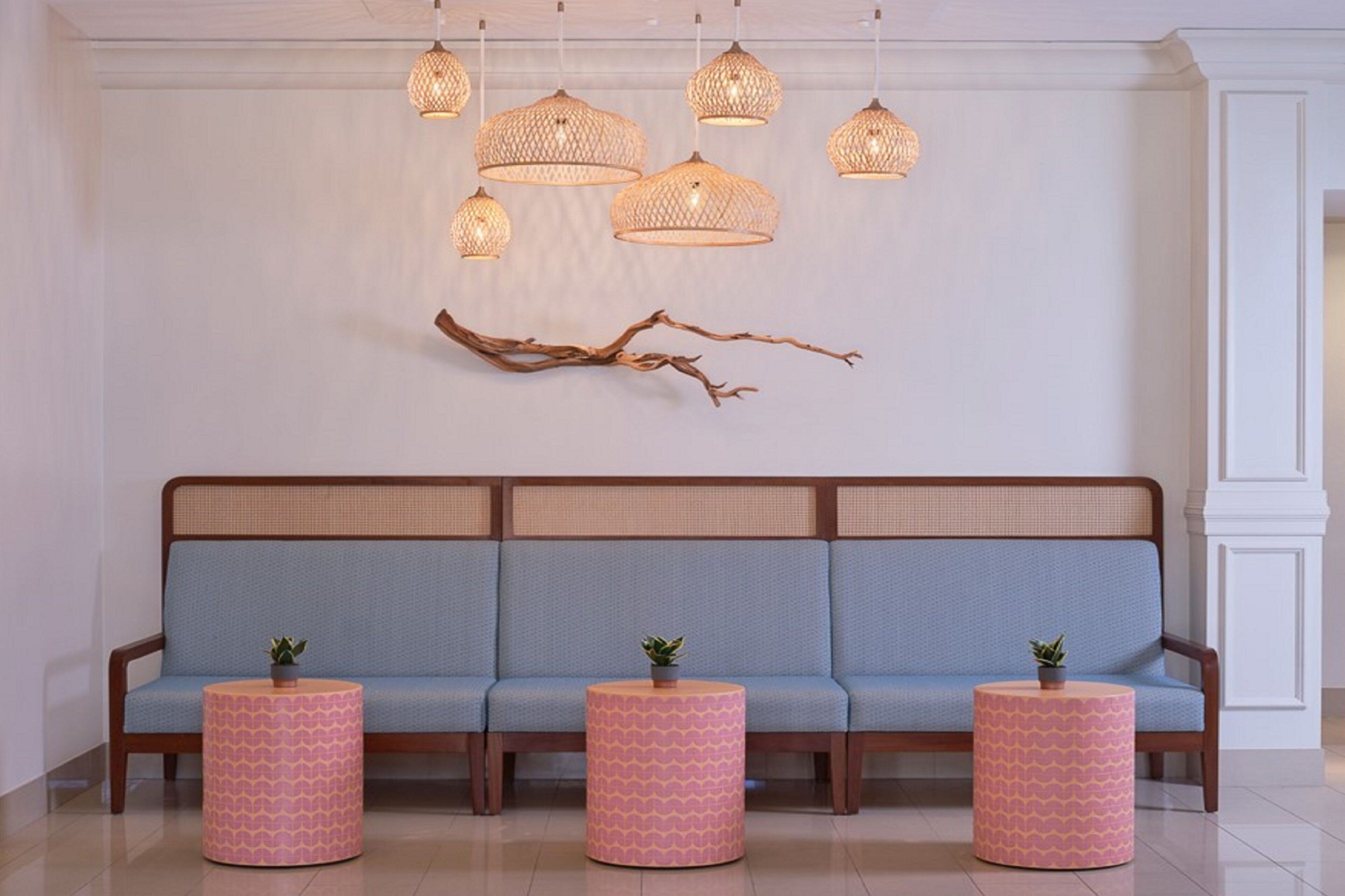 A modern lobby with a blue sofa, pink patterned side tables, and decorative hanging lights.