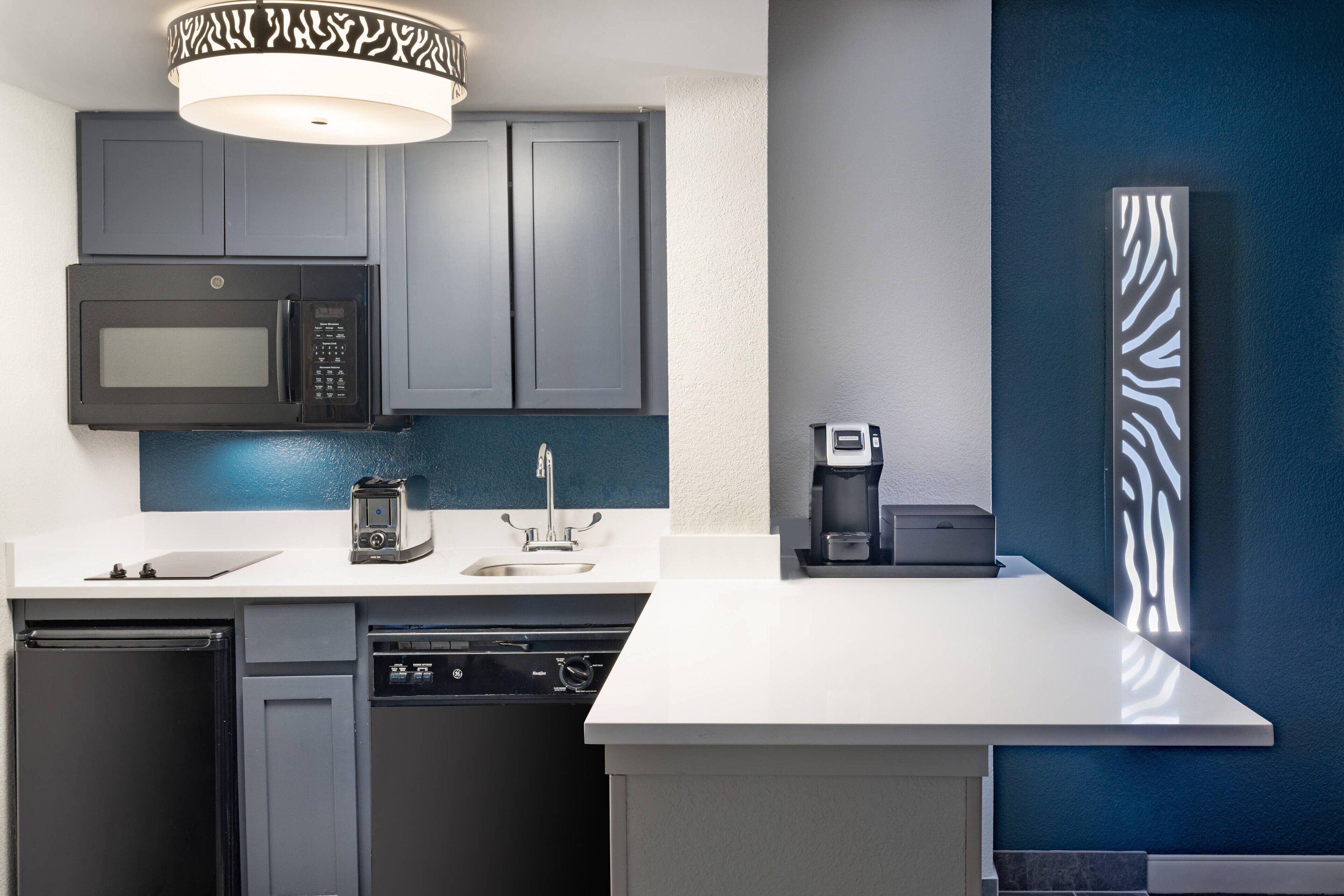 A modern kitchen with grey cabinets, a white countertop, a built-in microwave, a coffee maker, and a dishwasher.