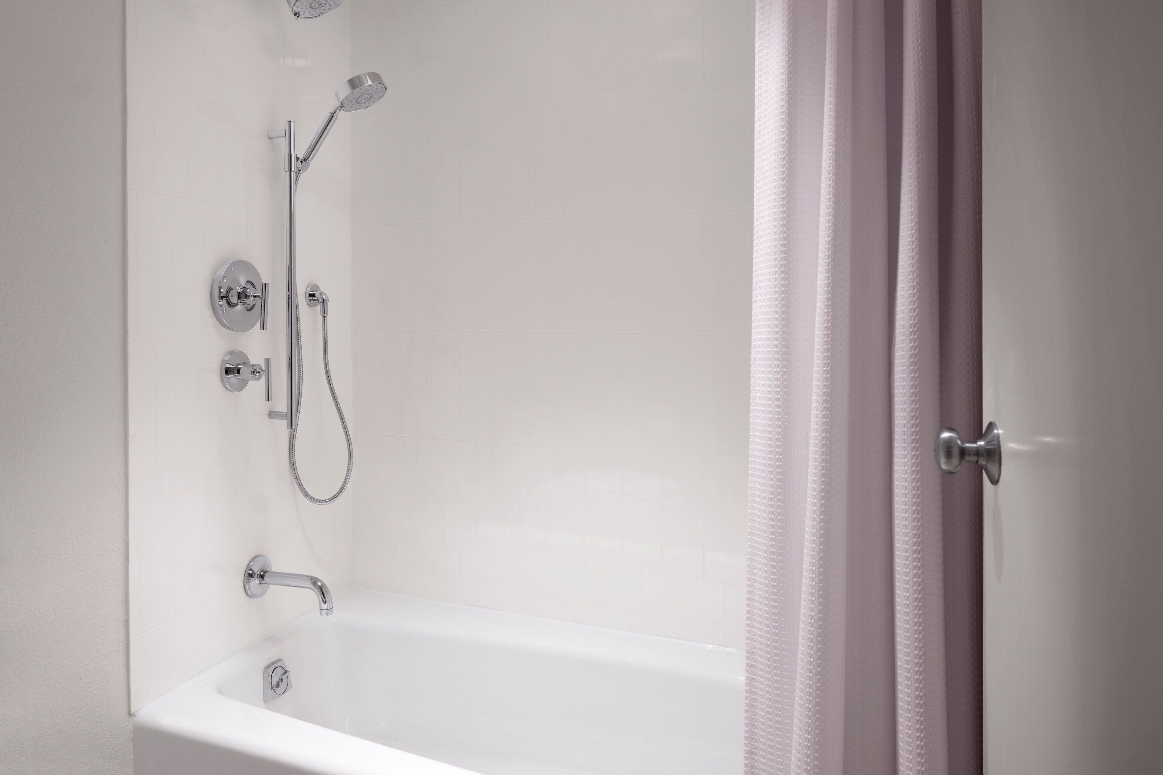 A modern bathroom with a white bathtub, a showerhead, and a handheld shower attachment.