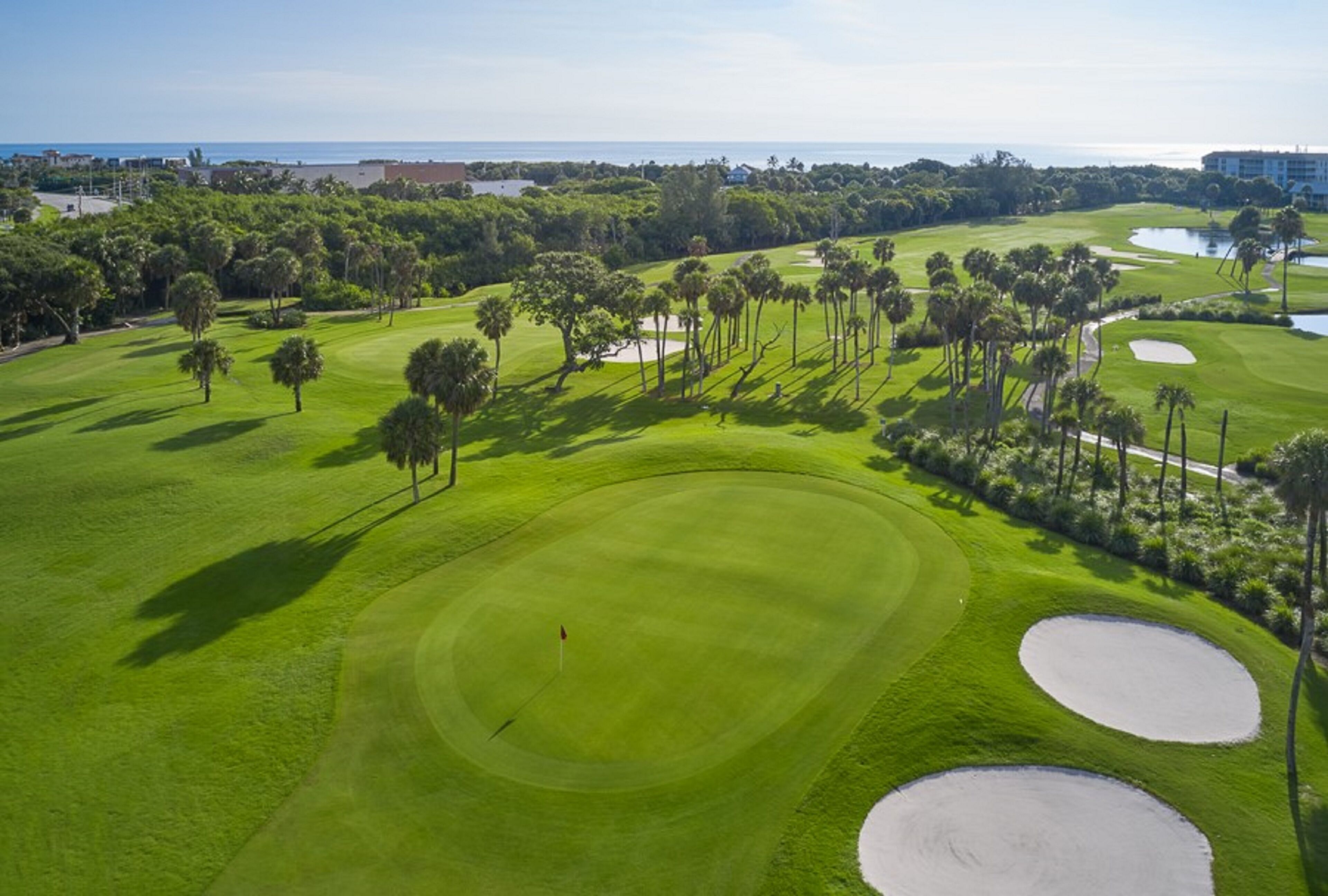 Vue aérienne d’un parcours de golf avec des allées bien entretenues, des bunkers de sable et un drapeau indiquant le trou.