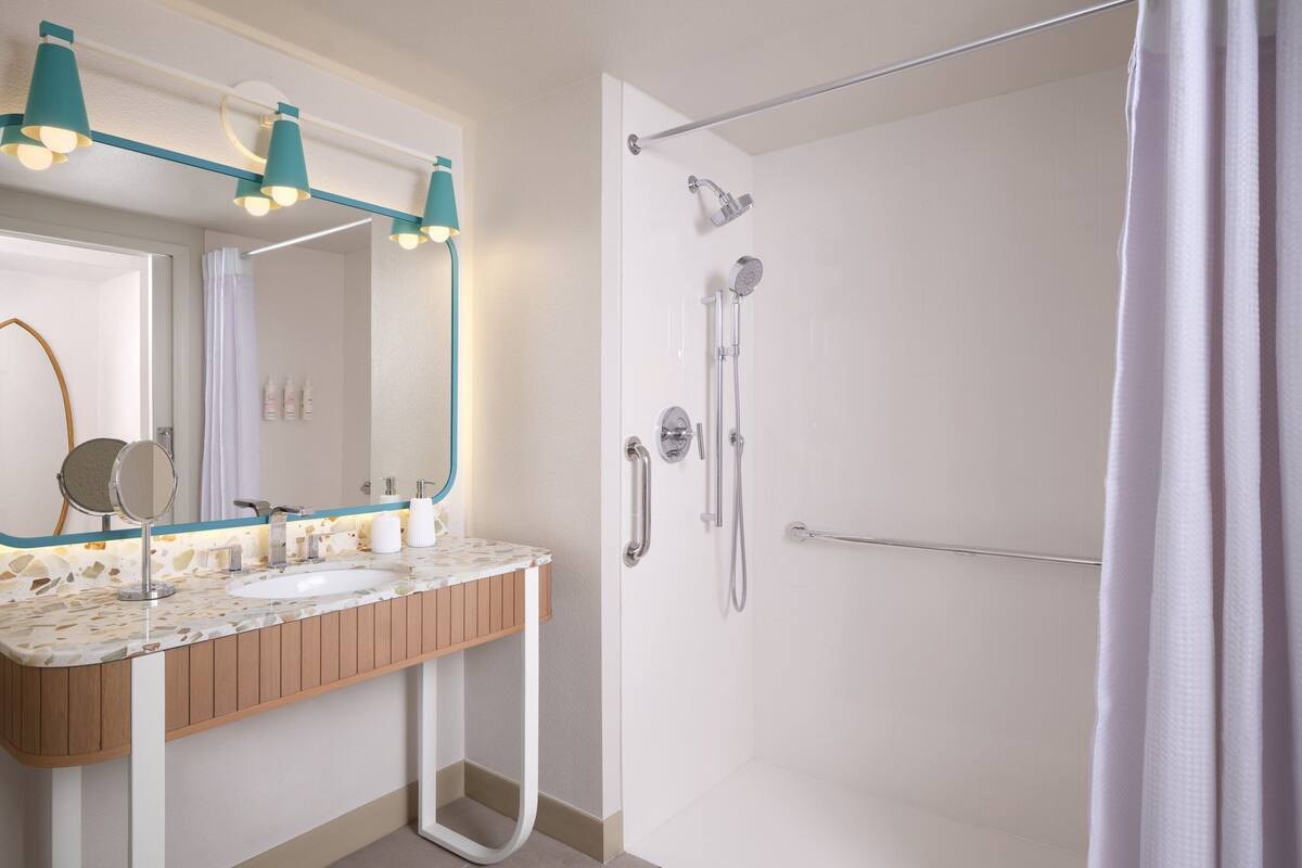 Un baño moderno con tocador de madera, un espejo grande y una ducha con puerta de cristal.