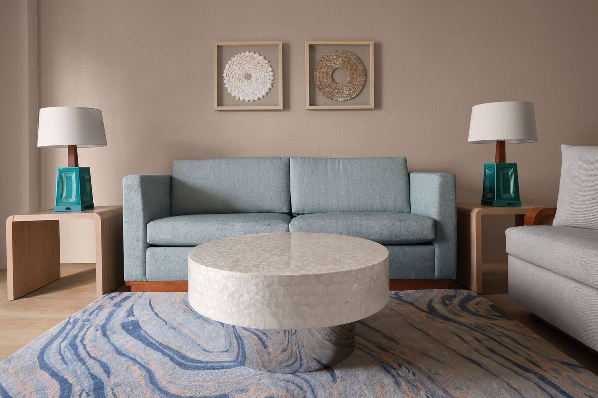 Una sala de estar con un sofá azul claro, dos mesitas de noche con lámparas turquesa, una mesa de centro redonda y dos obras de arte enmarcadas colgadas en la pared.
