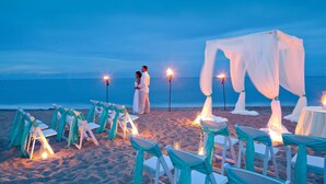 Decoración para una boda en la playa, con sillas y mesas blancas, una carpa y antorchas.