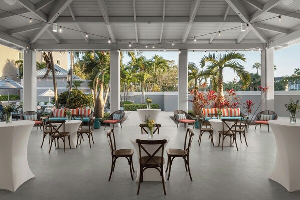Un patio al aire libre con mobiliario blanco, incluyendo sofás y sillones, dispuestos alrededor de una mesa central.