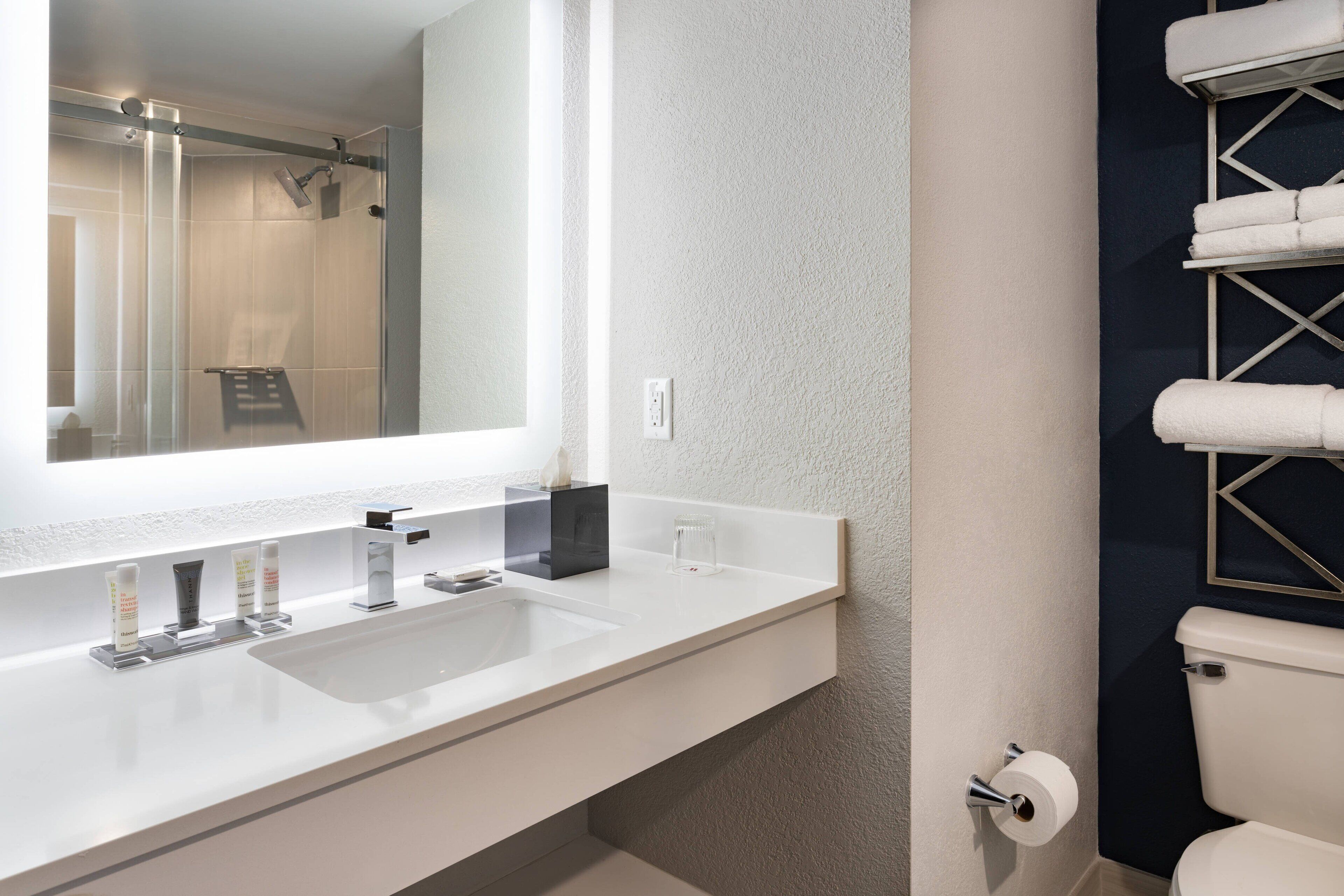 Un baño moderno con un espejo grande, un lavamanos blanco y una cabina de ducha de vidrio.