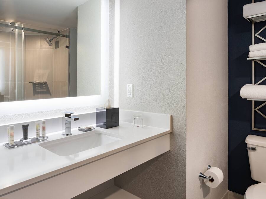 A modern bathroom with a large mirror, white sink, and a glass shower enclosure.