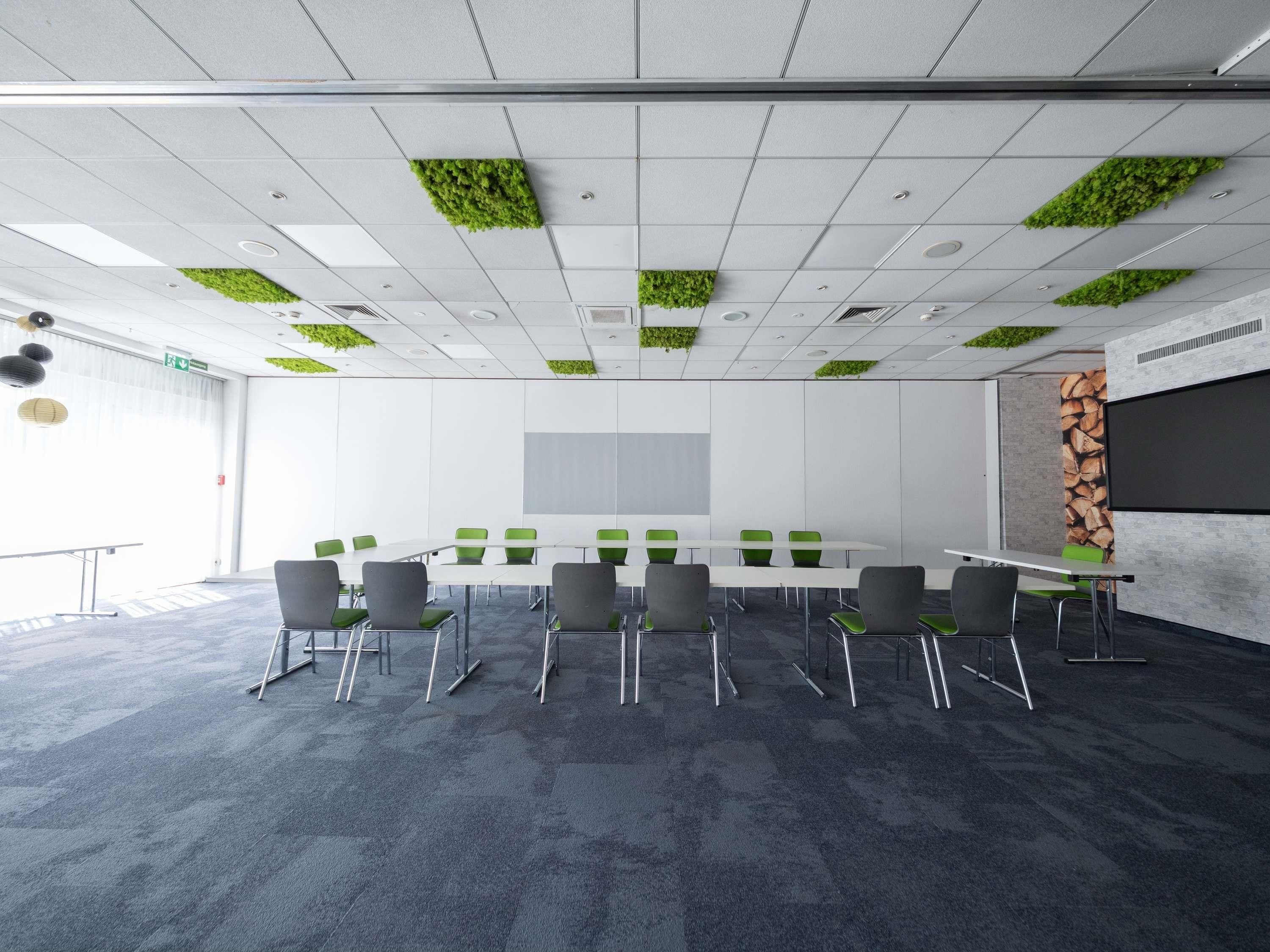 Un salón de conferencias con una larga mesa, sillas, una pantalla de proyector e instalaciones de plantas verdes en el techo.