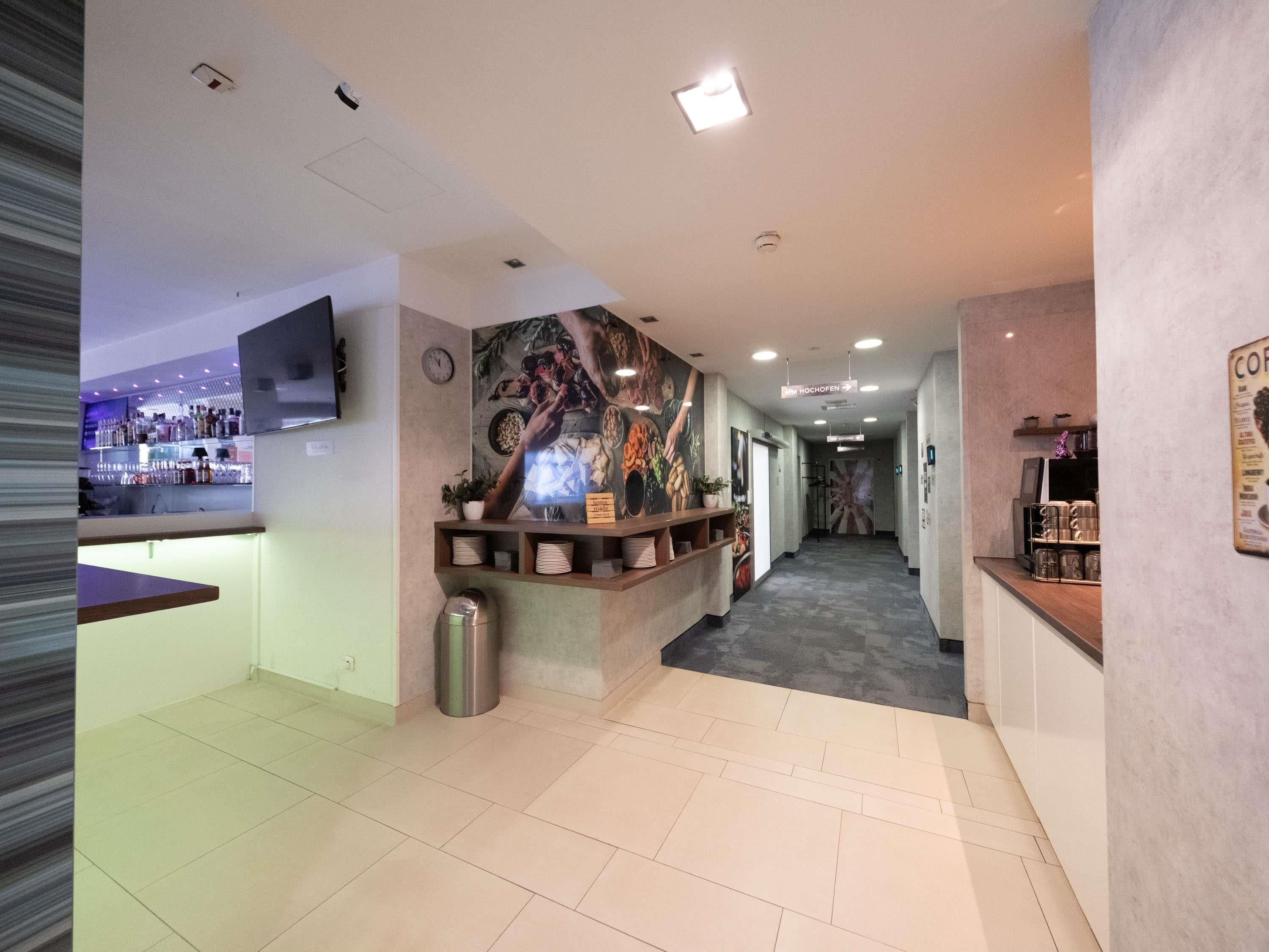 A hotel lobby with a reception desk, a bar area, and a hallway leading to other rooms.