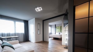 Una habitación de hotel moderna con sofá, una mesa de comedor y un ventanal grande.