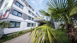 A modern building with a geometric facade, a green signboard, and a pathway leading to the entrance. - ibis Styles Linz (Linz)
