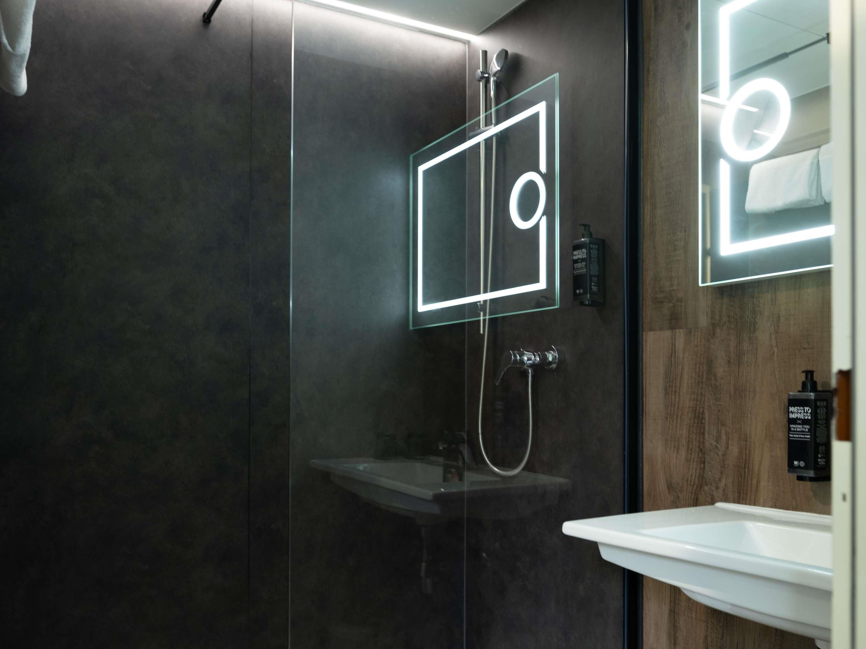 A modern bathroom with a glass-enclosed shower, a white sink, and a mirror with a neon light.