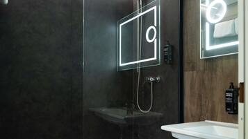 A modern bathroom with a glass-enclosed shower, a white sink, and a mirror with a neon light.