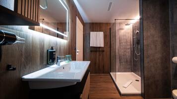 A modern bathroom with a wooden vanity, a large mirror, a shower, and a towel rack.