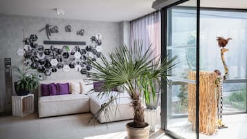 Una sala de estar moderna con un sofá gris, una planta grande en maceta y una pared decorada con marcos hexagonales para fotos.