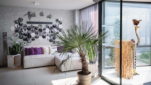 Una sala de estar moderna con un sofá gris, una planta grande en maceta y una pared decorada con marcos hexagonales para fotos.