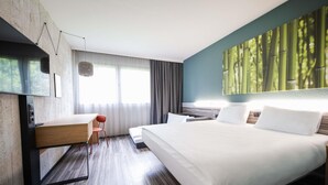 A modern hotel room with a large bed, a desk, and a television.