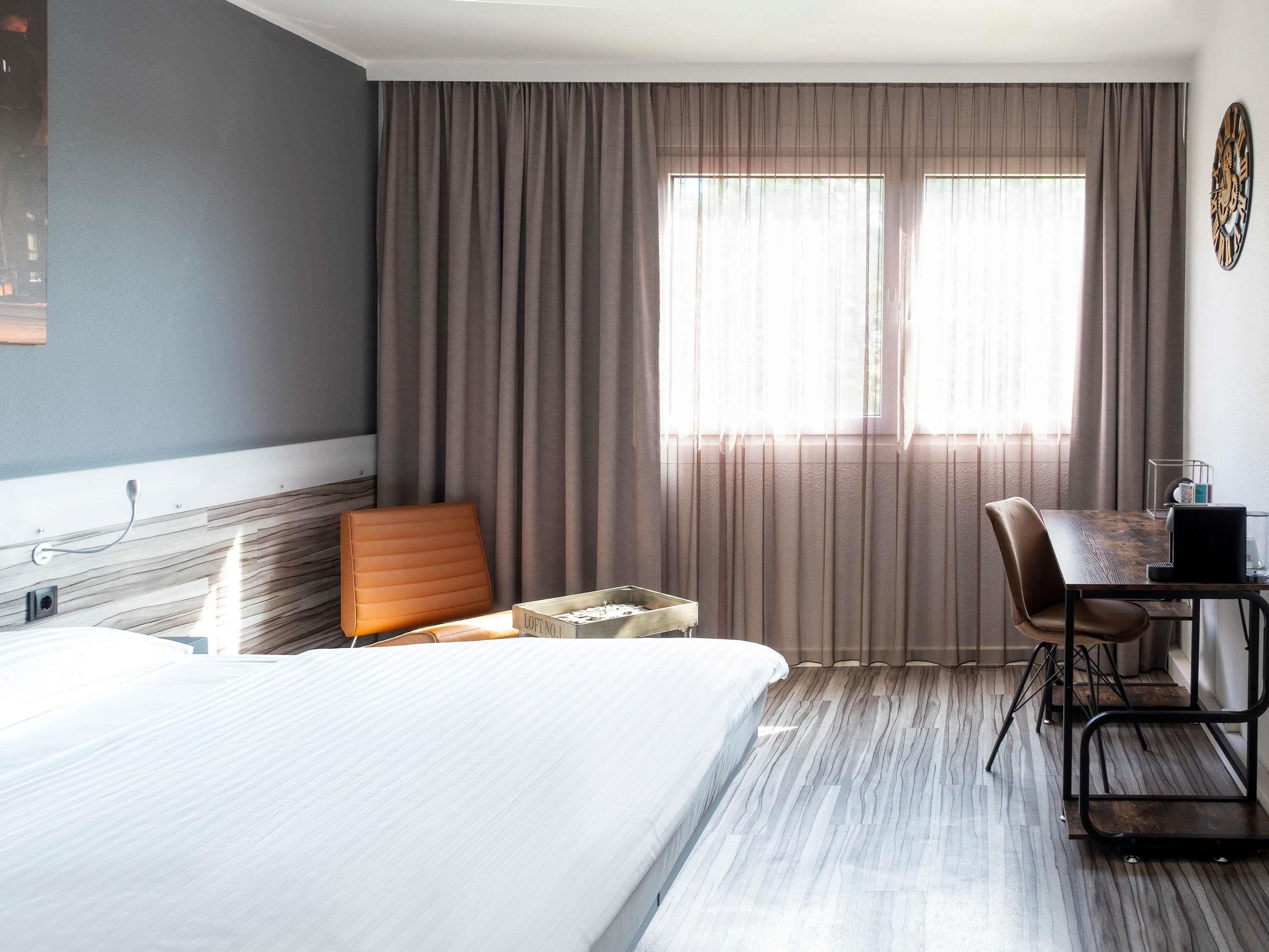 A hotel room with a bed, a desk, a chair, and a window with curtains.