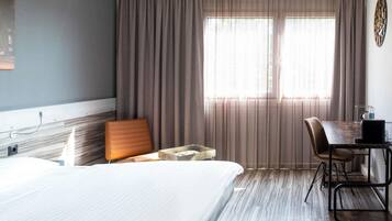 A hotel room with a bed, a desk, a chair, and a window with curtains.