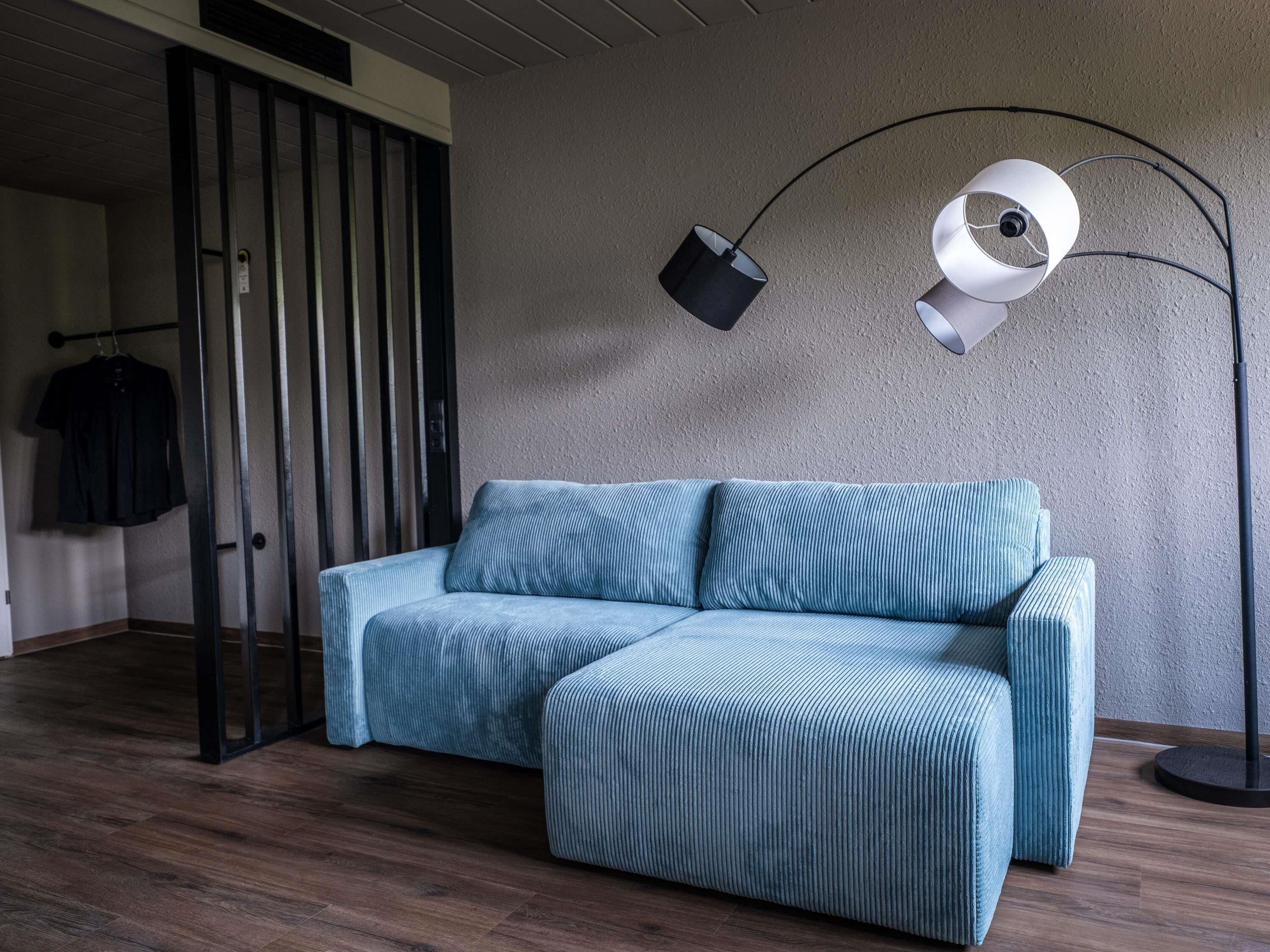 A modern living room with a blue sofa, a floor lamp, and a wooden floor.