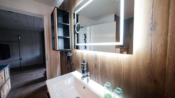 A modern bathroom with a white sink, wooden paneling, a mirror with integrated lighting, and a hairdryer.