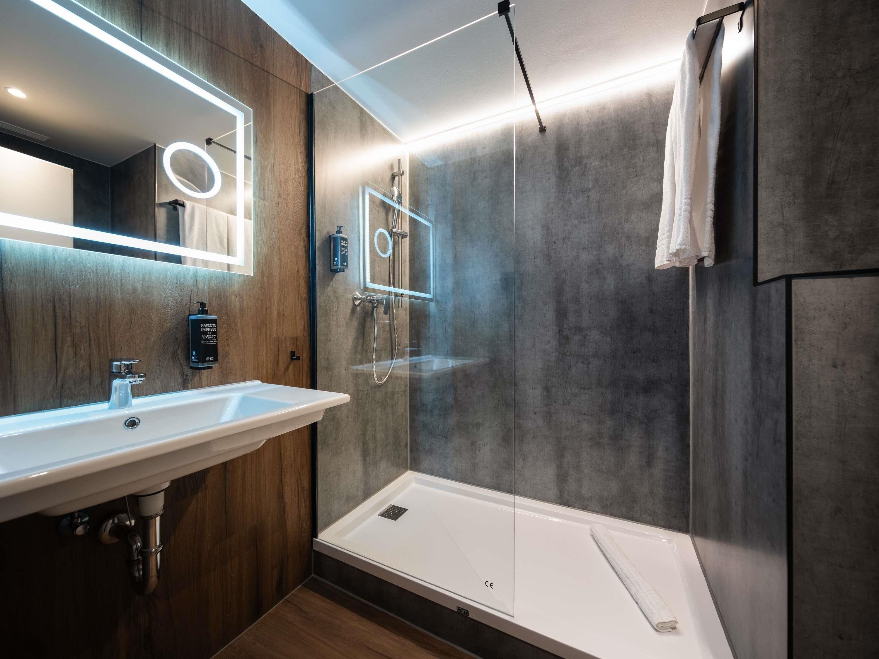 Un baño moderno con tocador de madera, cabina de ducha de vidrio y bañera blanca.
