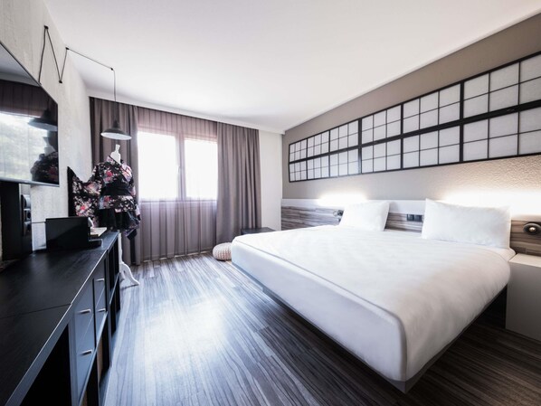 A modern hotel room with a large bed, a desk with a computer, and a view of the city.