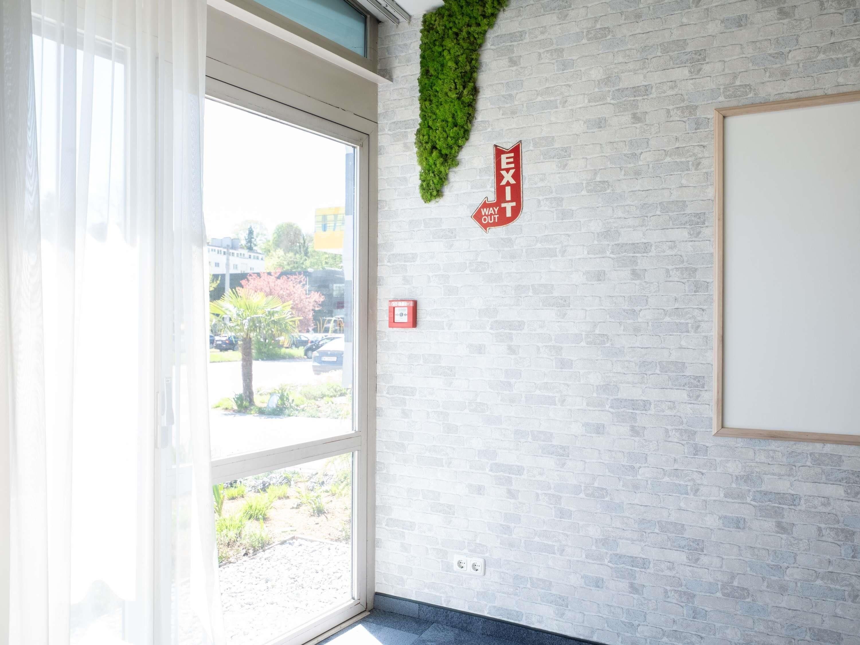 Ein Zimmer mit Backsteinwand, einem Vorhangfenster und einem Fluchtwegschild.