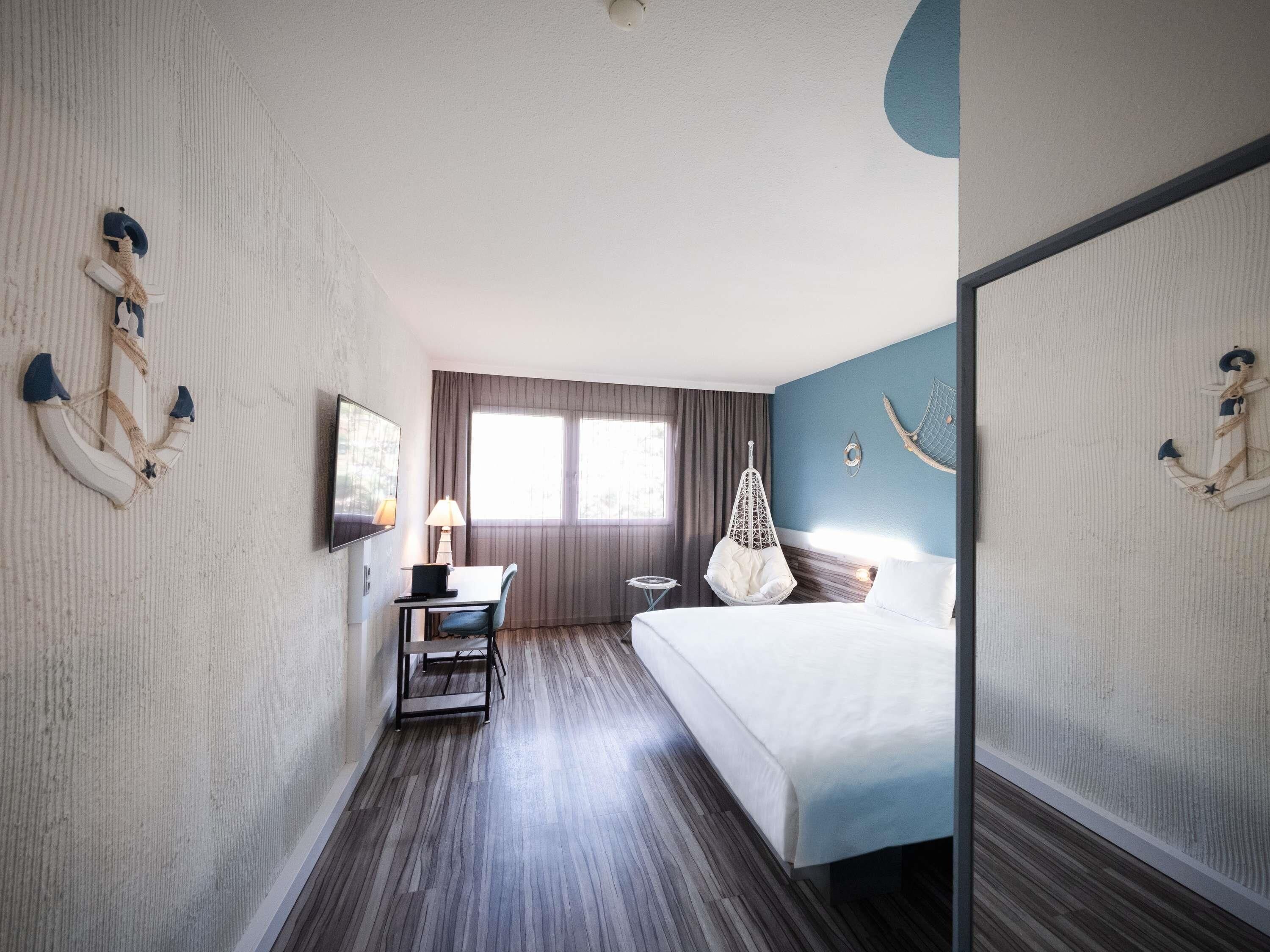 Habitación de hotel con cama, escritorio, silla, sillón colgante y decoración náutica.