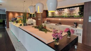 A modern reception area with a long counter, decorative plants, and a large wall mural. - ibis Styles Linz (Linz)