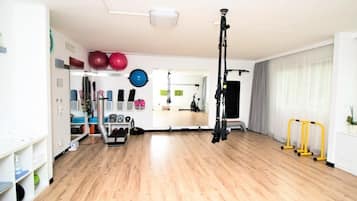 A spacious room with a wooden floor, exercise equipment, and a large window with curtains.