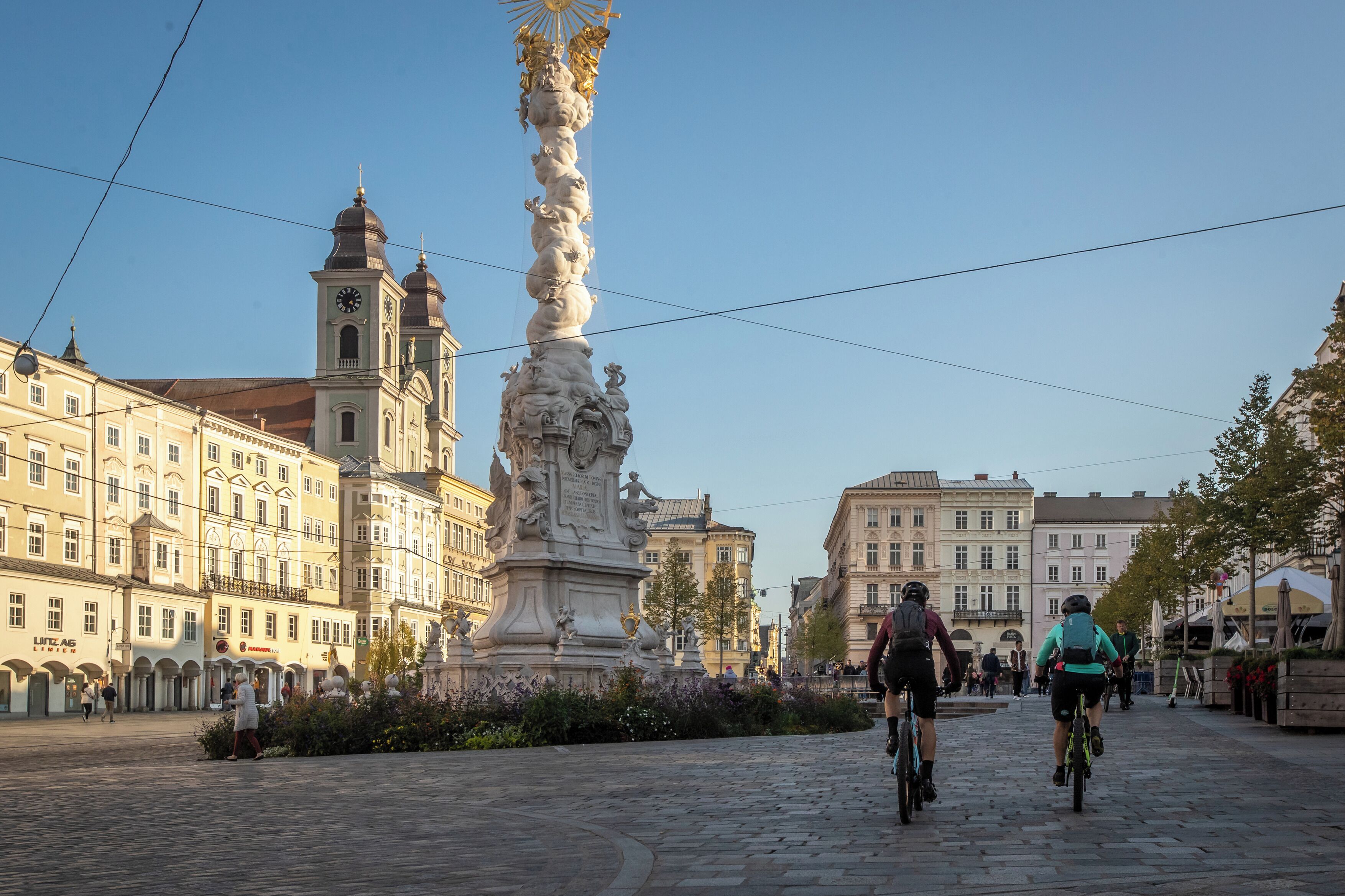 A cobblestone street with cyclists, historic buildings, and a prominent statue.