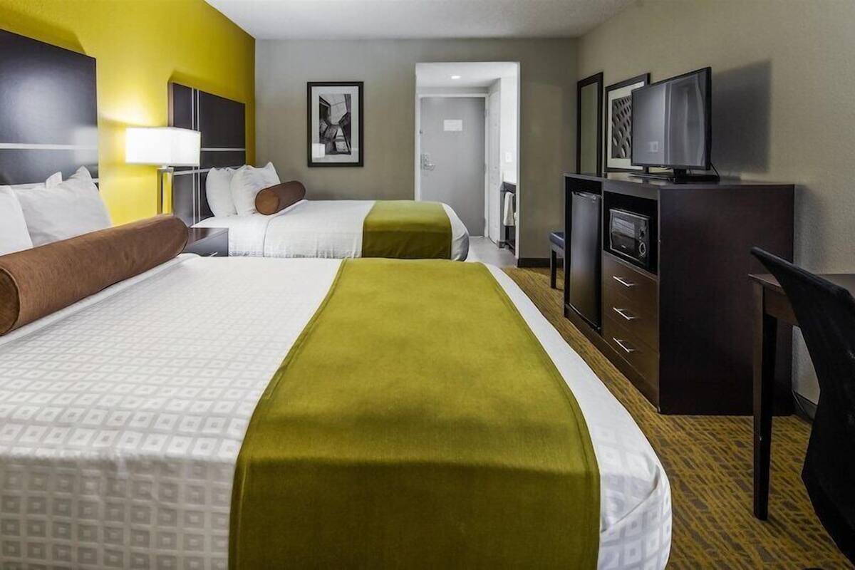 Een hotelkamer met twee bedden, een bureau, een televisie en een deur naar een andere kamer.
