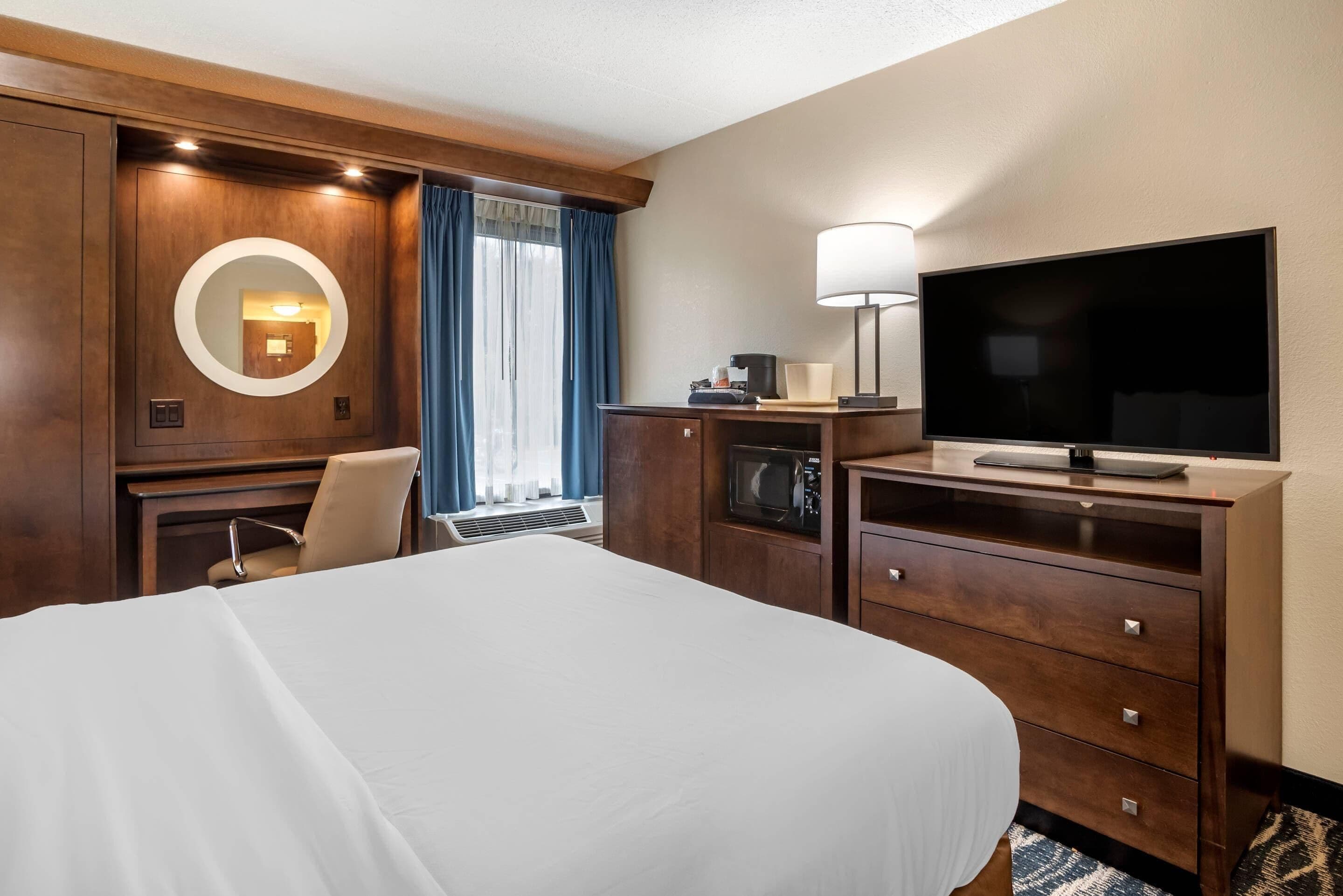 Una camera d'albergo con un letto grande, una scrivania con lampada, una TV a schermo piatto e un forno a microonde.