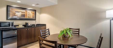 Habitación de hotel con kitchenette, una mesa de comedor con sillas, una planta en maceta y un cuadro en la pared.
