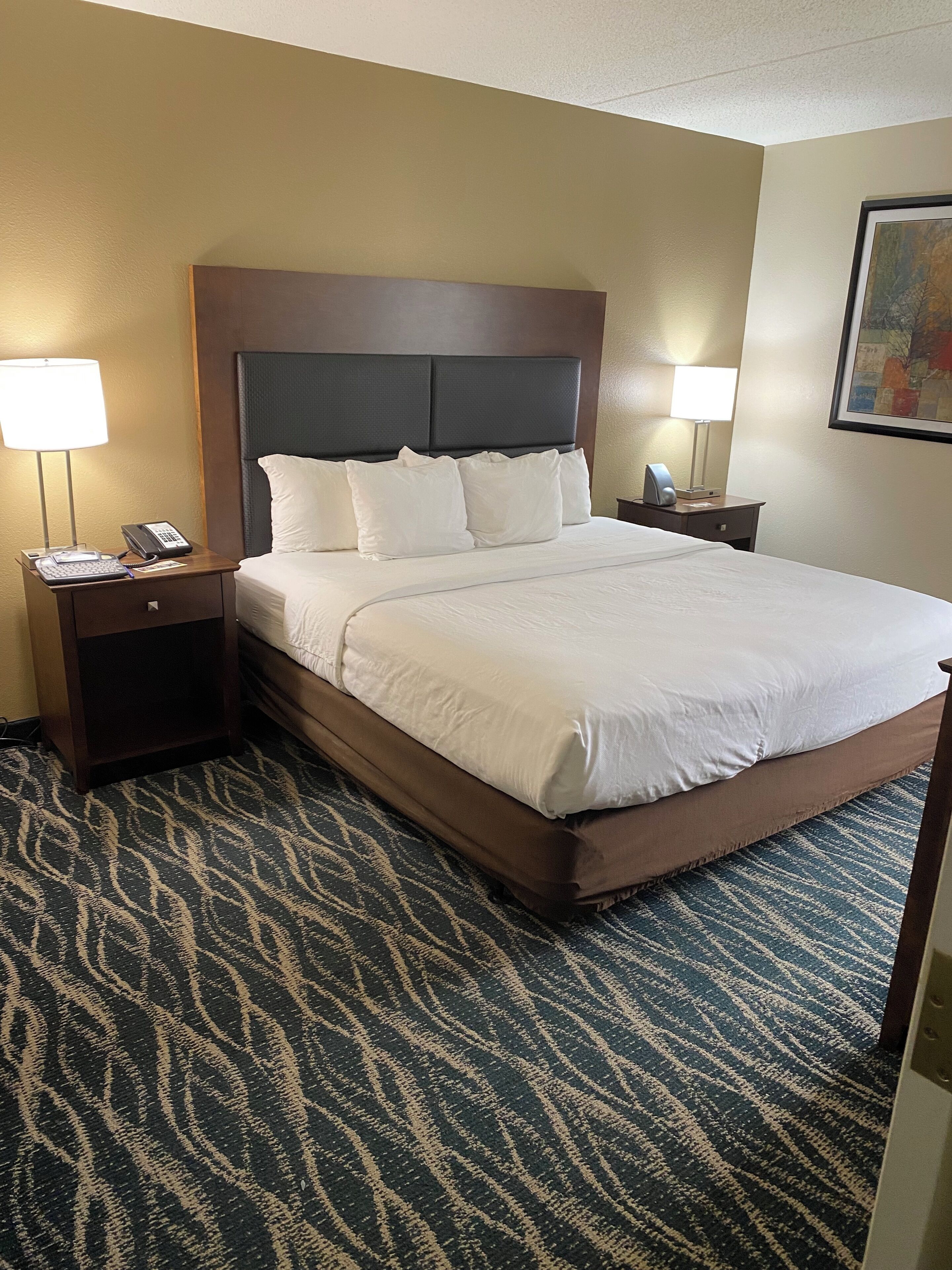 Quarto de hotel com uma cama grande, duas mesas de cabeceira, um telefone e uma luminária em cada lado.
