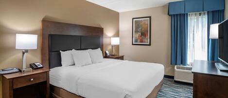 Habitación de hotel con una cama grande, dos mesitas de noche con lámparas, un escritorio con computadora, un televisor y una ventana con cortinas.