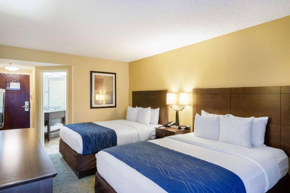 A hotel room with two beds, a desk, and a bathroom visible through an open door.
