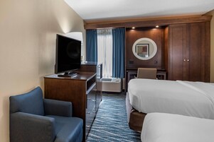 Una habitación de hotel con cama, escritorio con televisor, silla, armario y piso alfombrado.